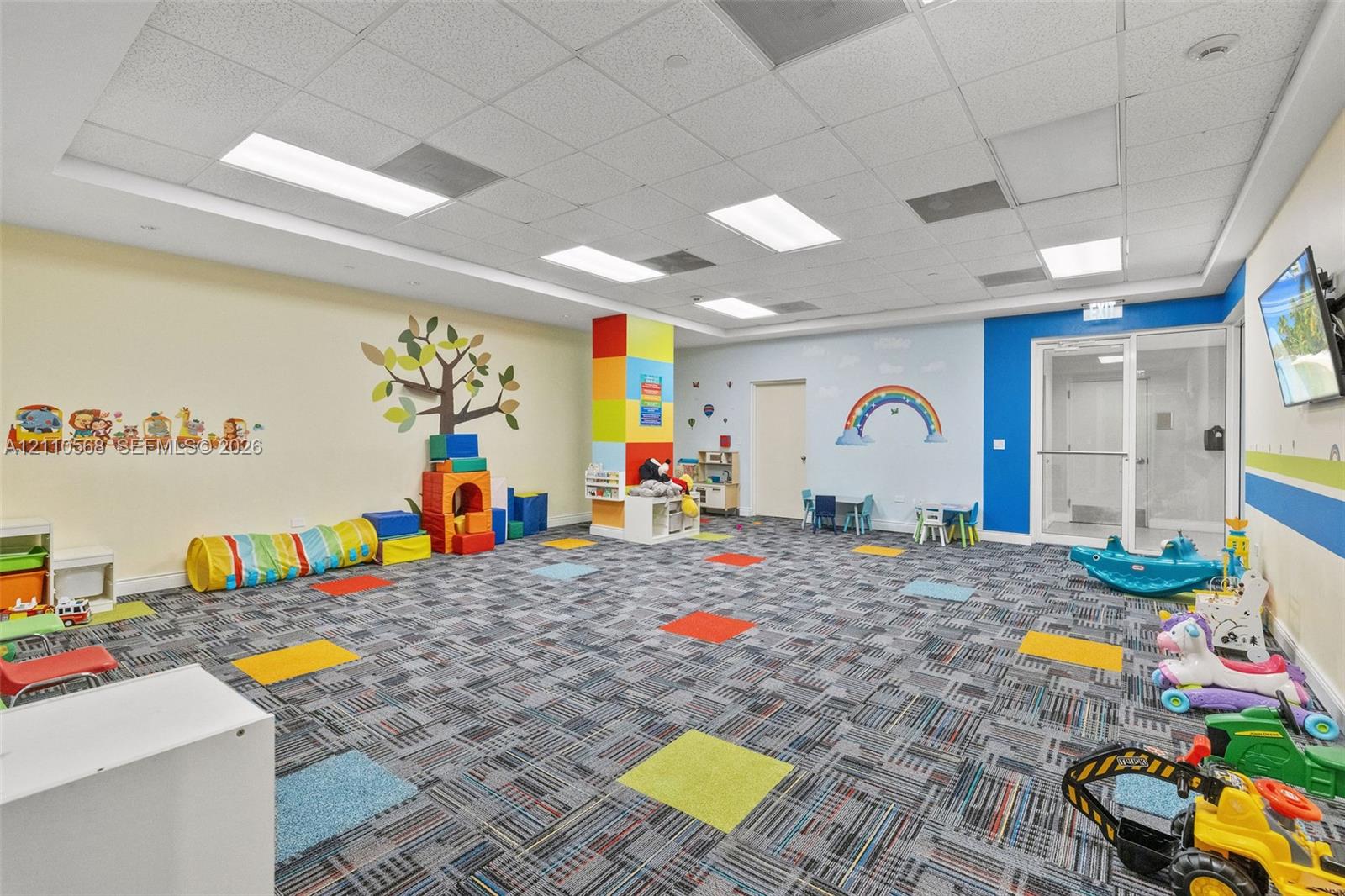 Multi-purpose room featuring a drop ceiling with recessed lighting, patterned carpet tiles, and glass entry doors