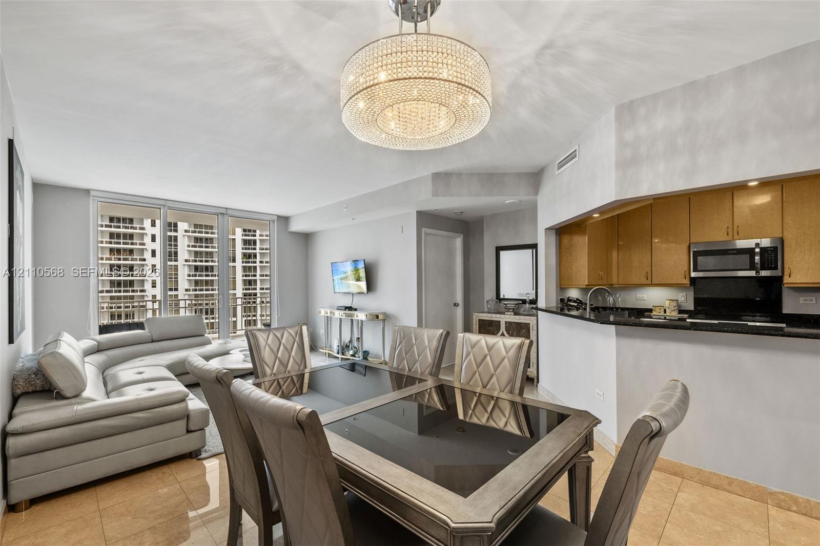 Open-concept interior featuring large-format tile flooring, a crystal drum chandelier, and expansive floor-to-ceiling windows