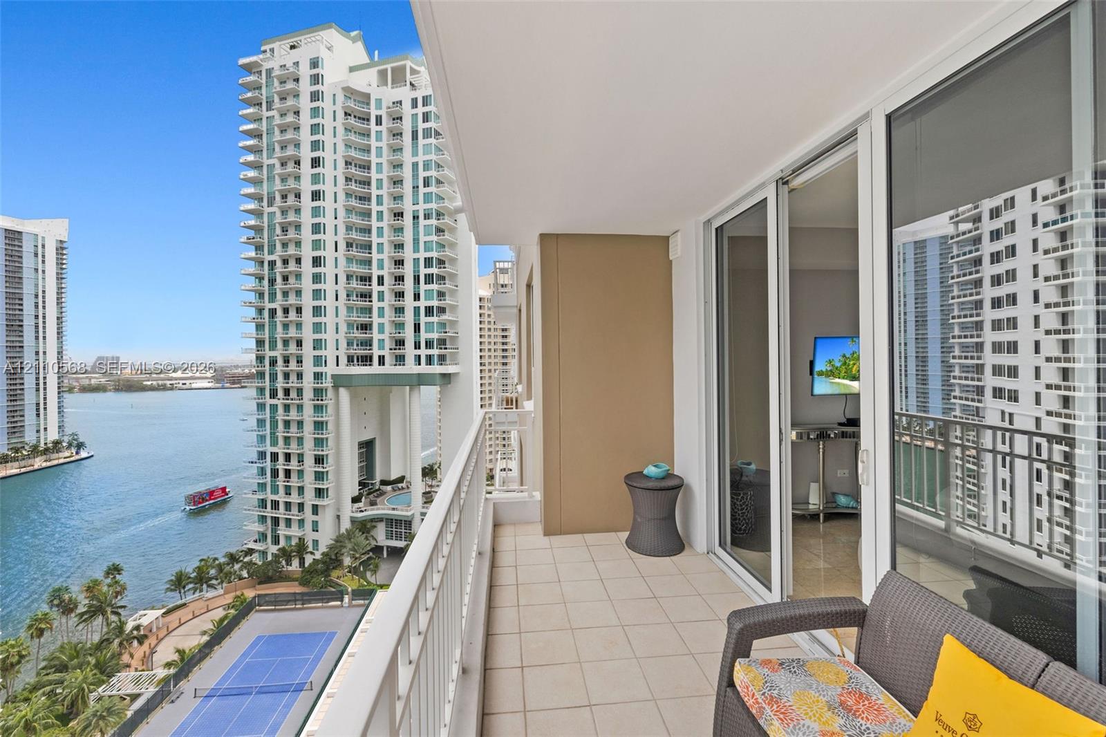 Private balcony featuring tile flooring and a metal railing, overlooking the water and tennis courts