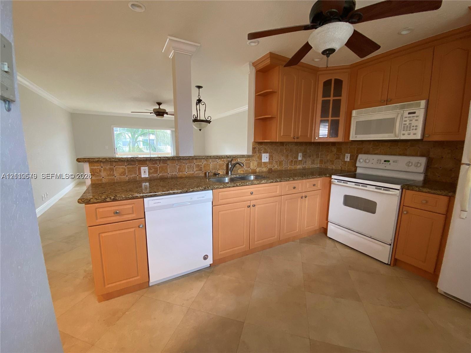 Kitchen featuring natural finish wood cabinetry, stone countertops, tiled backsplash, neutral tone tile flooring, and a ceiling-mounted fan with integrated lighting Kitchen featuring natural finish wood cabinetry, stone countertops, tiled backsplash, neutral tone tile flooring, and a ceiling-mounted fan with integrated lighting
