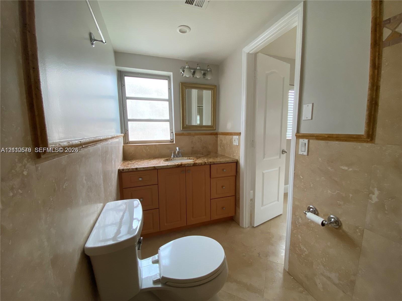 Bathroom featuring stone-tile wall wainscoting, wood-finish cabinetry, natural stone countertop, undermount sink, and wall-mounted vanity mirror