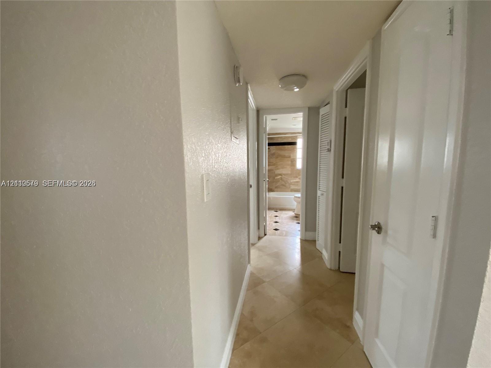 Hallway featuring diagonal tile flooring, smooth-finish walls, multiple panel doors, and a ceiling-mounted light fixture