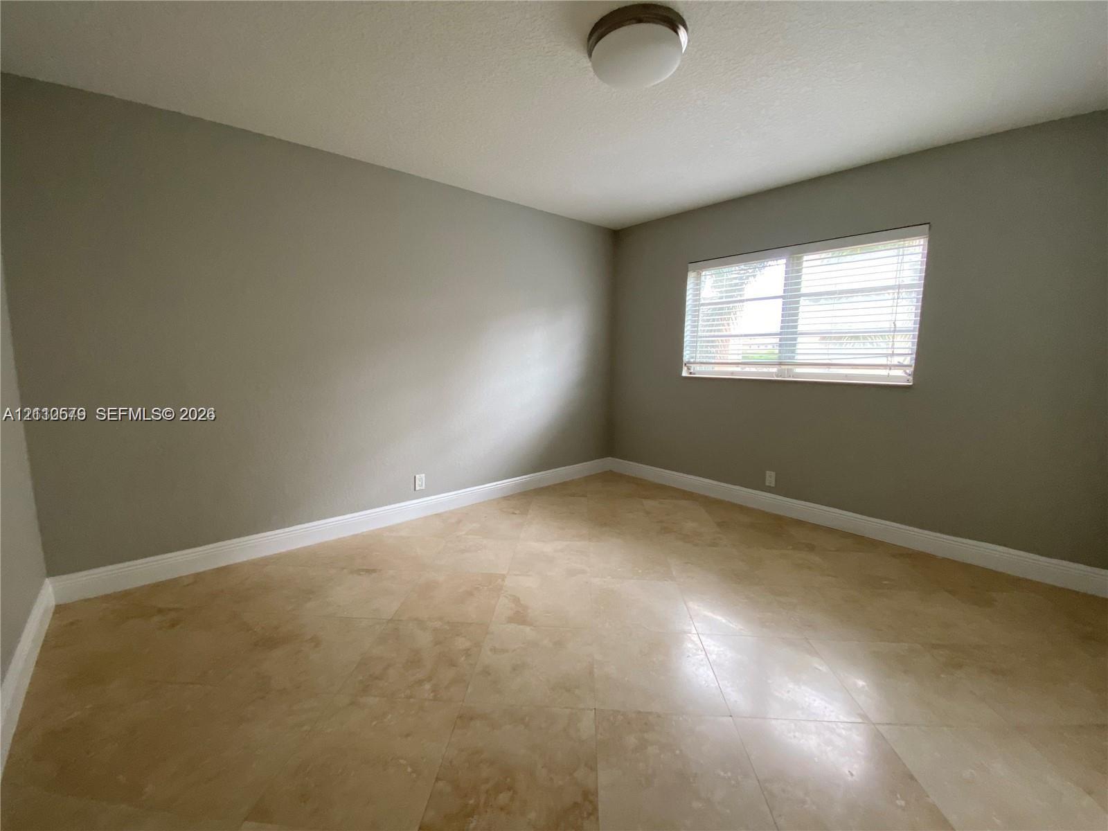 Neutral interior space featuring stone tile flooring, a window with horizontal blinds, and a flush-mount ceiling light