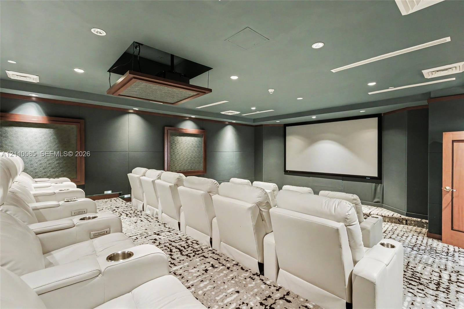 Media room featuring a fixed projection screen, ceiling-mounted projector, tiered floor levels, recessed lighting, and integrated wall paneling