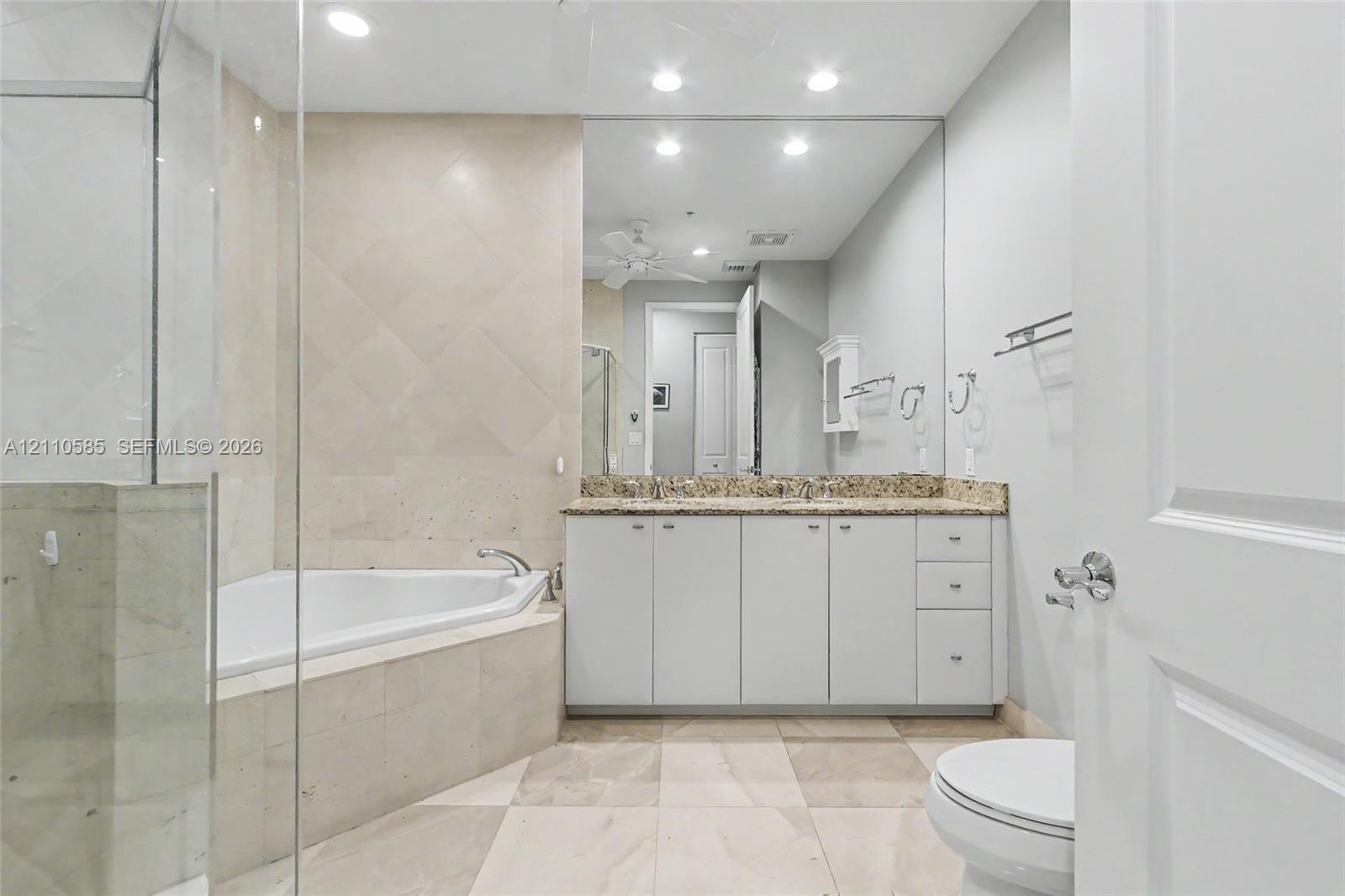 Main Bathroom featuring a double-sink vanity with stone countertop, corner soaking tub with tile surround, glass-enclosed shower, and large wall-mounted mirror