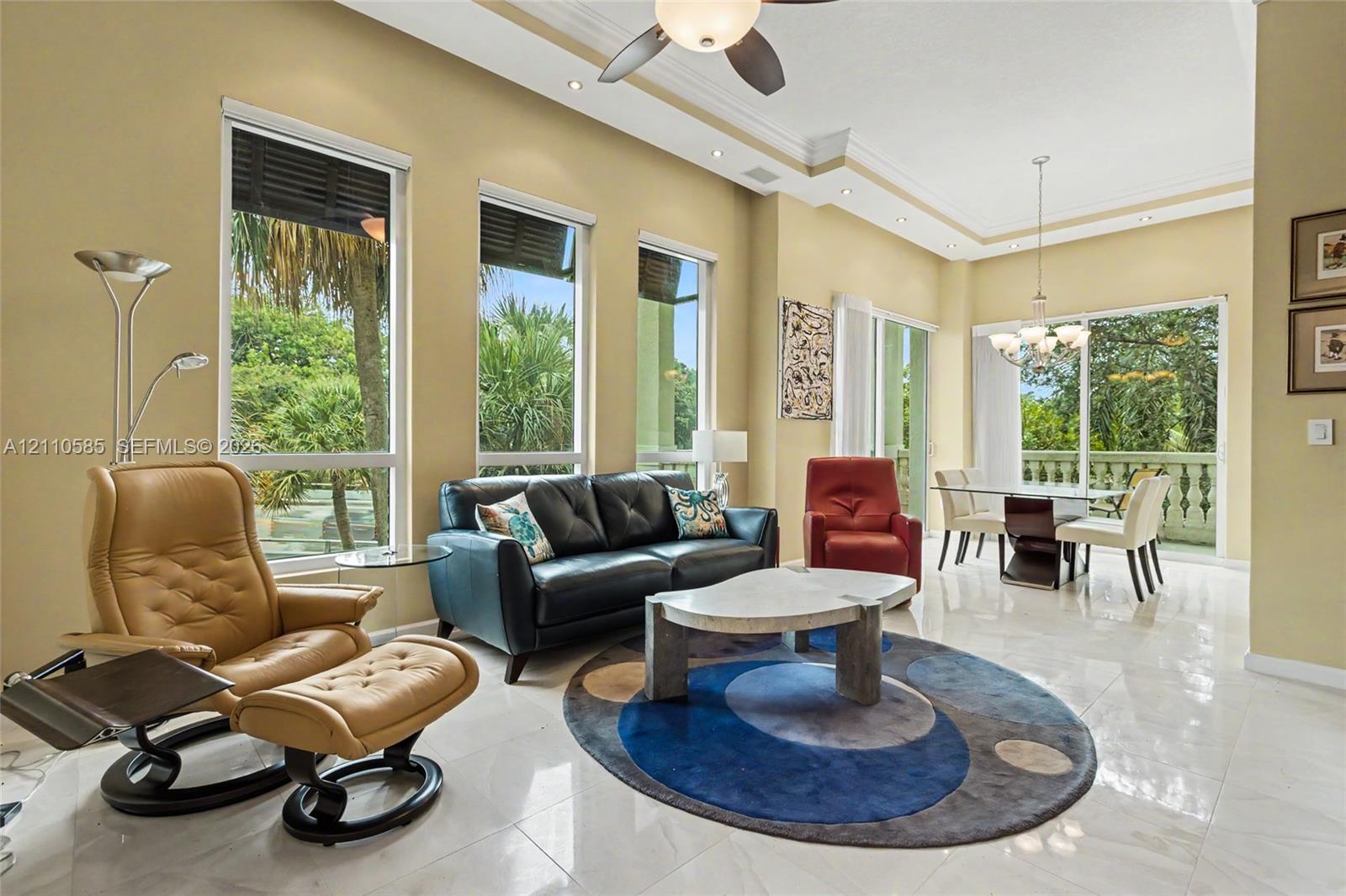 Open-concept living space featuring high ceilings with crown molding, large-format tile flooring, recessed lighting, and expansive windows providing natural light
