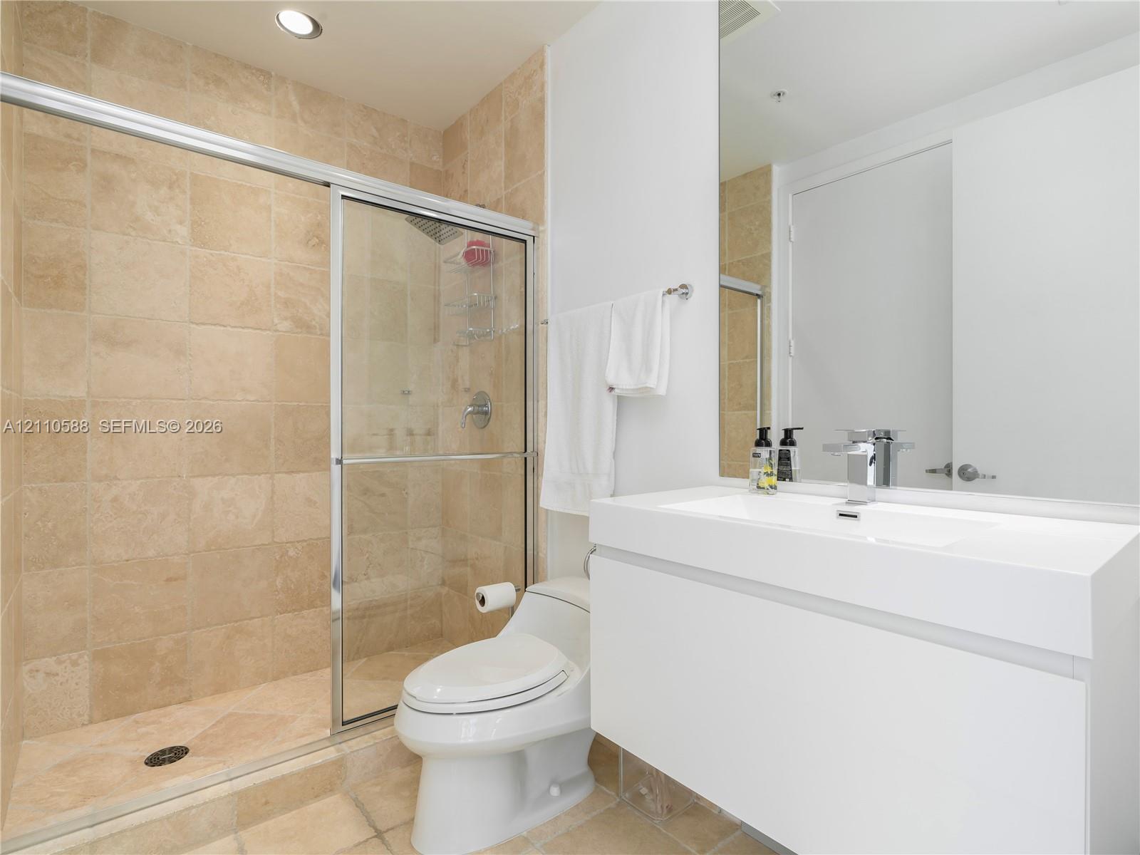 Modern wall-mounted vanity with a rectangular sink, stone-tiled walk-in shower with a glass enclosure, and large-format wall mirror