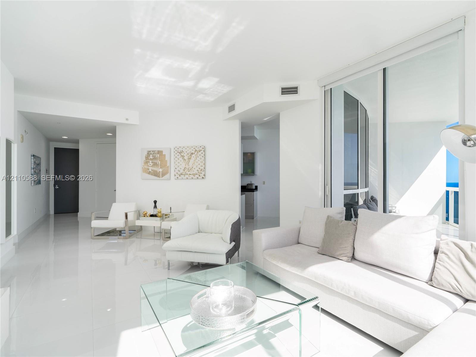 Open-concept living space with polished tile flooring, recessed ceiling lighting, and floor-to-ceiling glass sliding doors opening to an exterior balcony