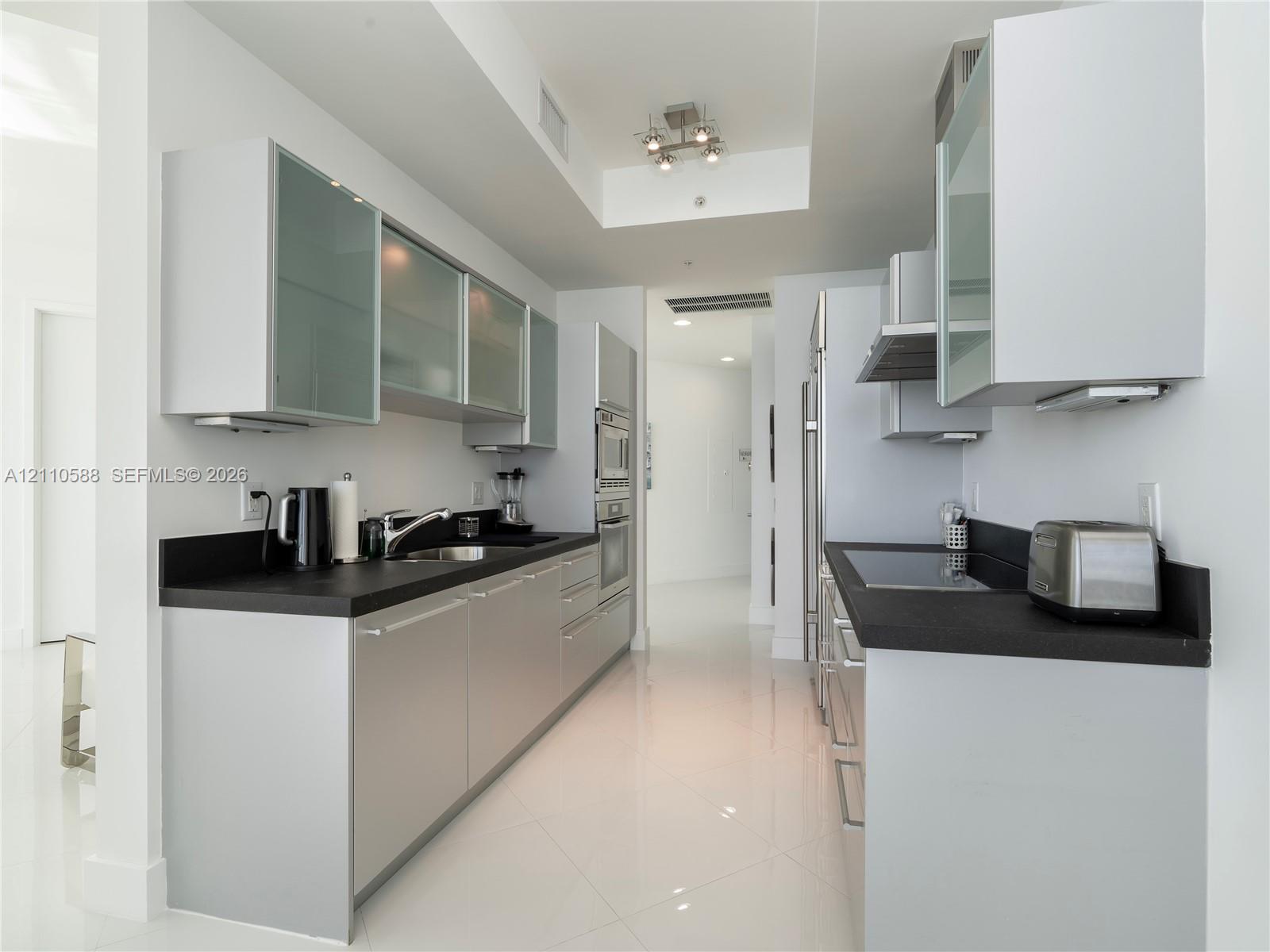 Contemporary kitchen featuring flat-panel cabinetry, frosted glass-front upper cabinets, contrasting dark countertops, integrated stainless steel appliances, and polished tile flooring