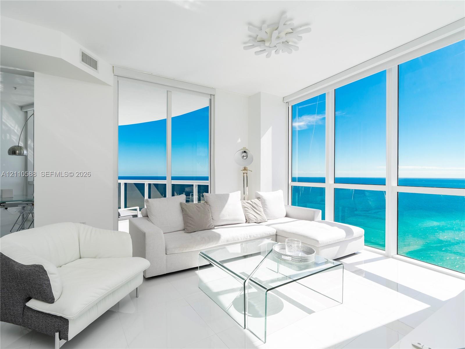 Floor-to-ceiling windows, white tile flooring, sliding glass door, white geometric ceiling fixture, and exterior balcony Floor-to-ceiling windows, white tile flooring, sliding glass door, white geometric ceiling fixture, and exterior balcony