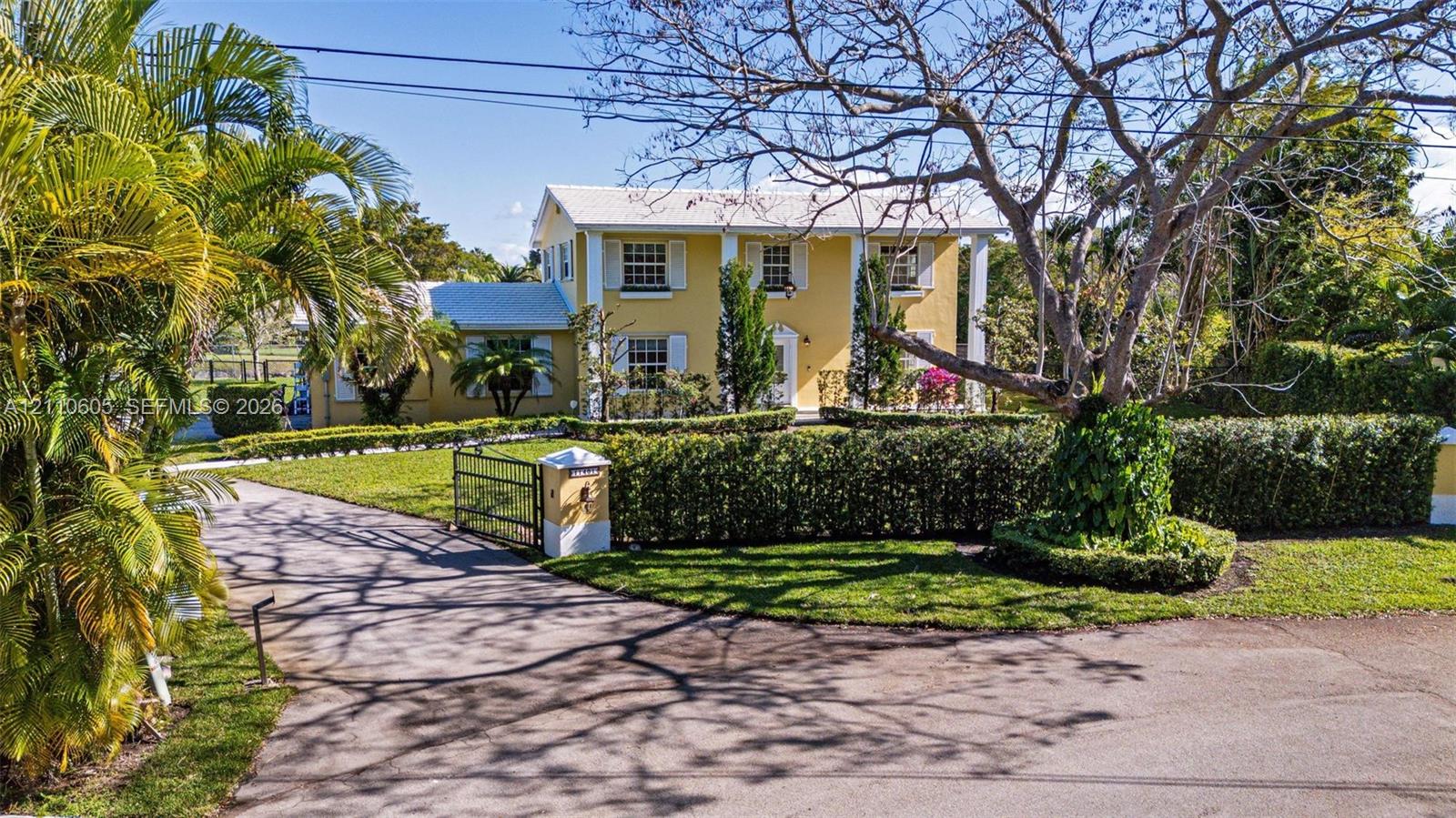 Two-story exterior featuring a columned facade, multi-pane windows with shutters, metal roof, paved driveway, and established landscape