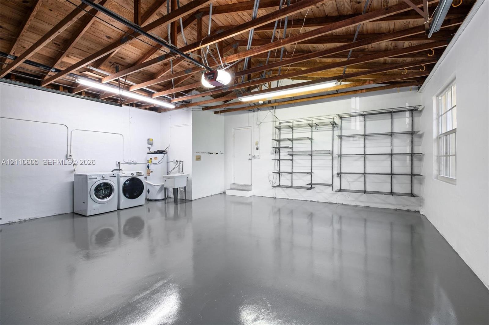 Garage space featuring an exposed wood truss ceiling, epoxy-finished flooring, wall-mounted metal shelving, and a utility sink