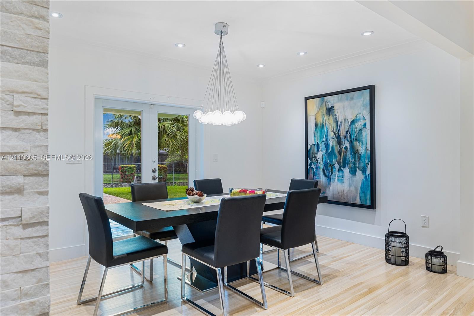 Stacked stone accent wall, multi-light modern chandelier, recessed lighting, and glass-paneled double doors featuring exterior access