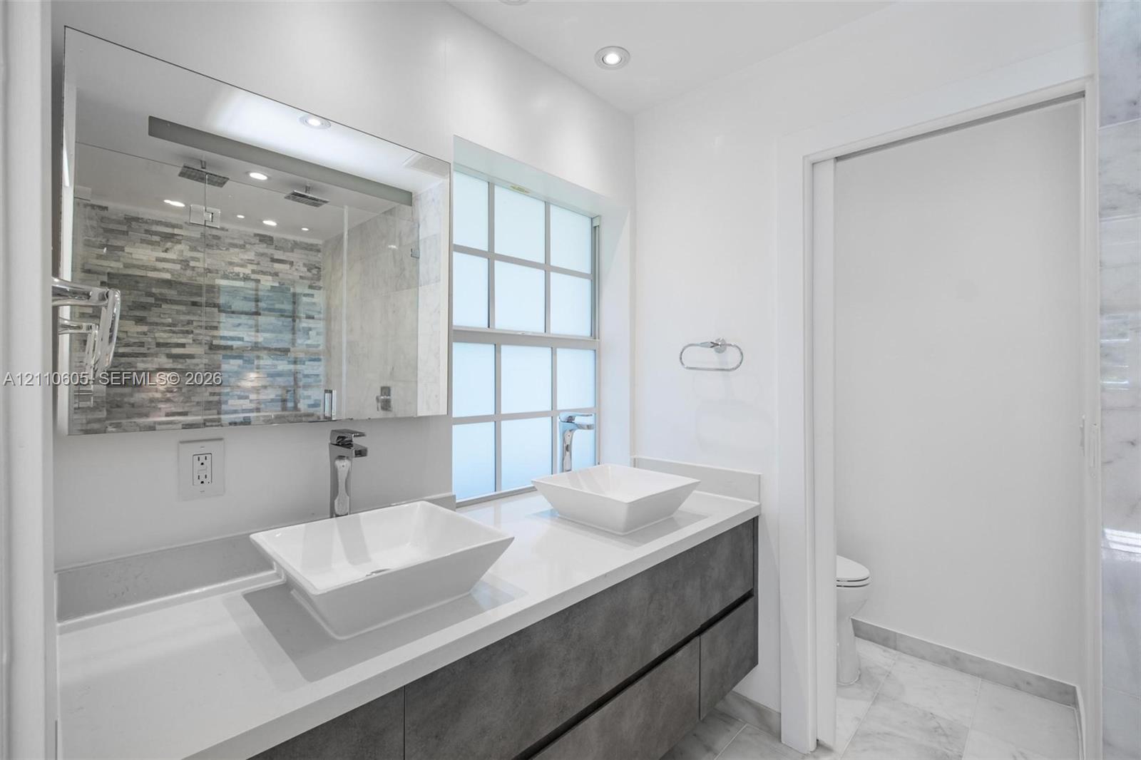 Floating dual-sink vanity with matte-finish cabinetry, white solid-surface countertops, rectangular vessel sinks, and a large frameless mirror