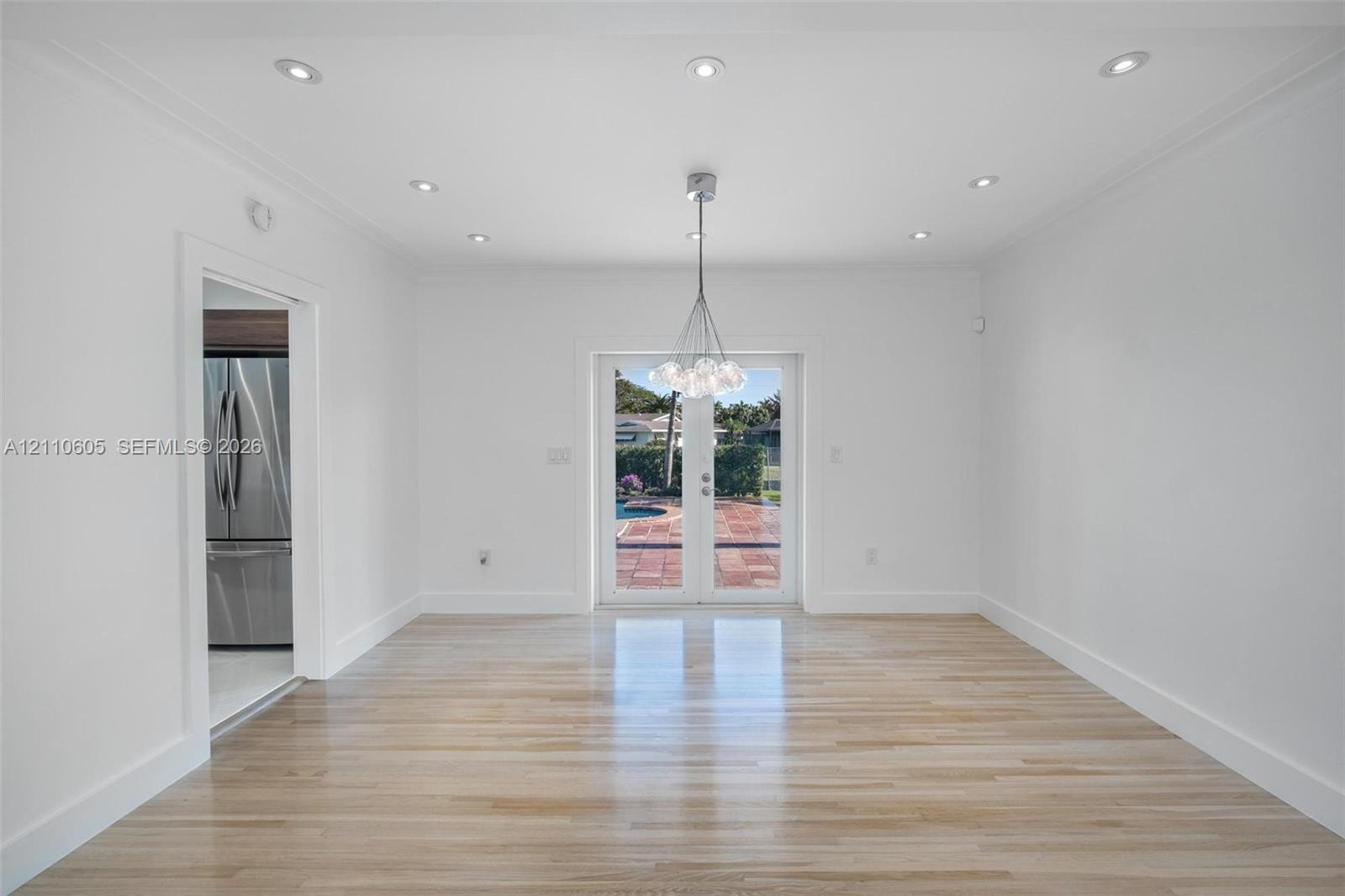Open-concept area featuring light wood-finish flooring, recessed lighting, a multi-bulb glass pendant fixture, and glass-paneled double doors