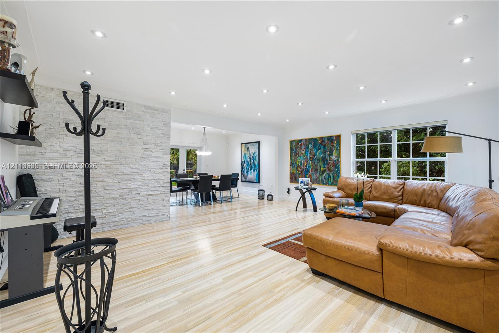 Open-concept interior featuring wood-finish flooring, a floor-to-ceiling stacked stone feature wall, recessed lighting, and multi-pane windows