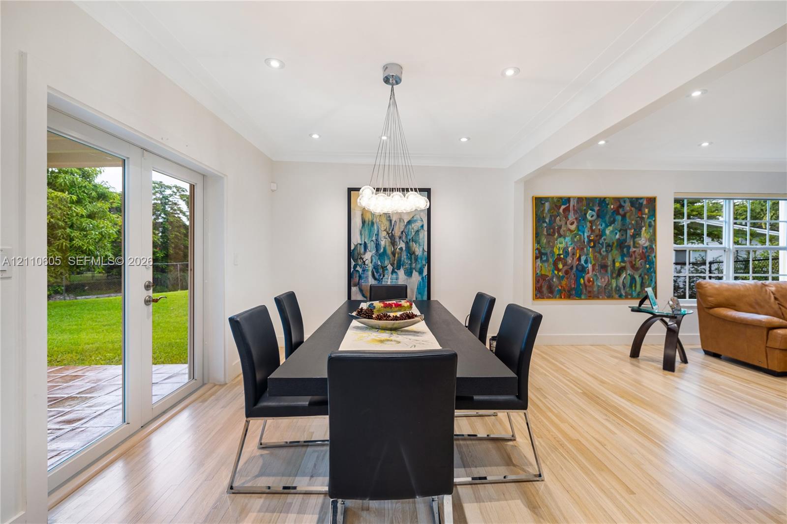 Dining area featuring light-toned wood-finish flooring, recessed lighting, a modern multi-light chandelier, and double glass-paneled doors providing exterior access