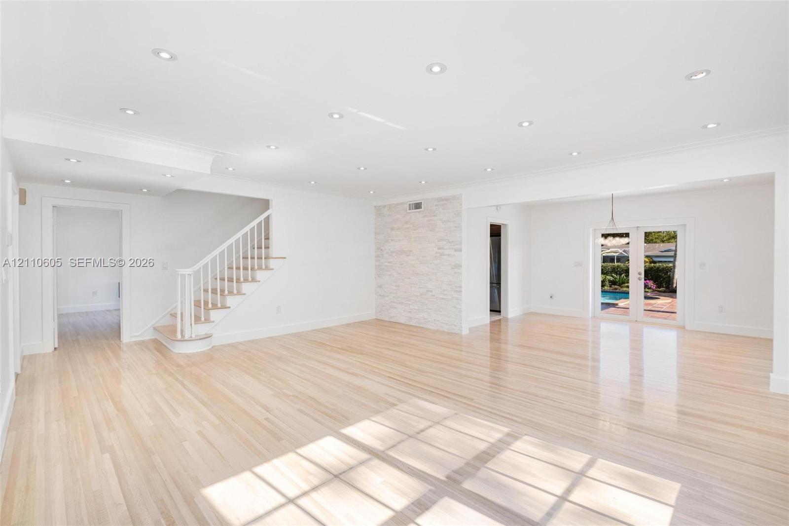 Open-concept interior featuring light wood-finish flooring, recessed lighting, a stone-accented wall, and white staircase railing