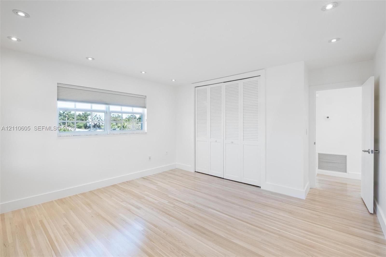 Neutral-toned interior featuring wood-finish flooring, recessed lighting, white louvered closet doors, and a window with a roller shade