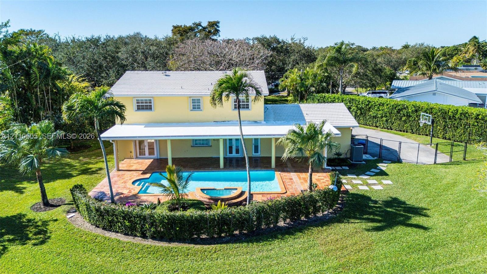 Two-story exterior featuring a covered patio, tiled pool deck, in-ground pool with integrated spa, and expansive lawn