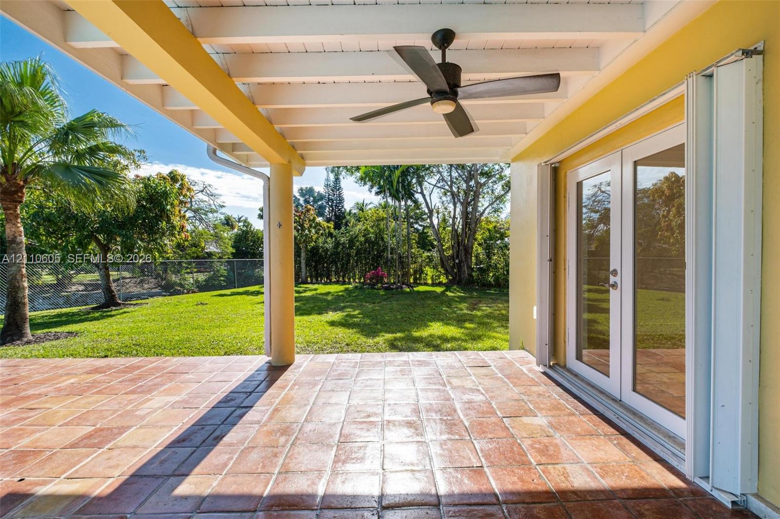 Covered patio featuring terra cotta tile flooring, a sloped wood-beam ceiling with a central fan, and double-glass paneled doors