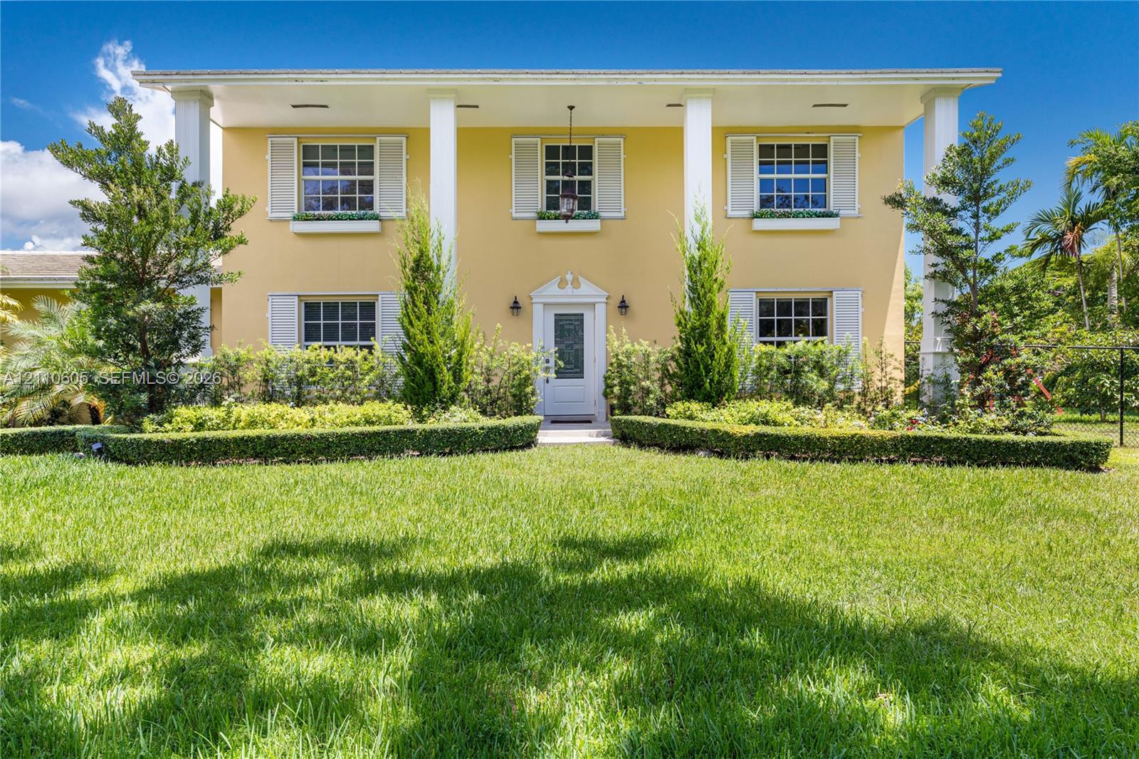 Two-story colonial exterior featuring a covered front porch, prominent structural columns, multi-pane windows with louvered shutters, and window box planters