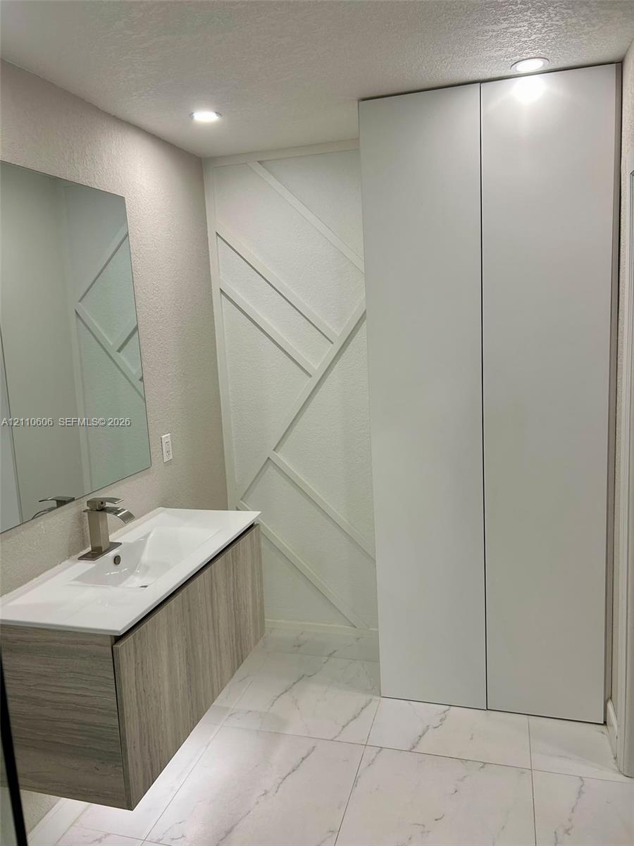 Floating vanity with wood-finish cabinetry, white countertop, integrated sink, and matte metallic faucet, complemented by full-height floor-to-ceiling cabinetry, geometric wall detailing, and large-format tile flooring