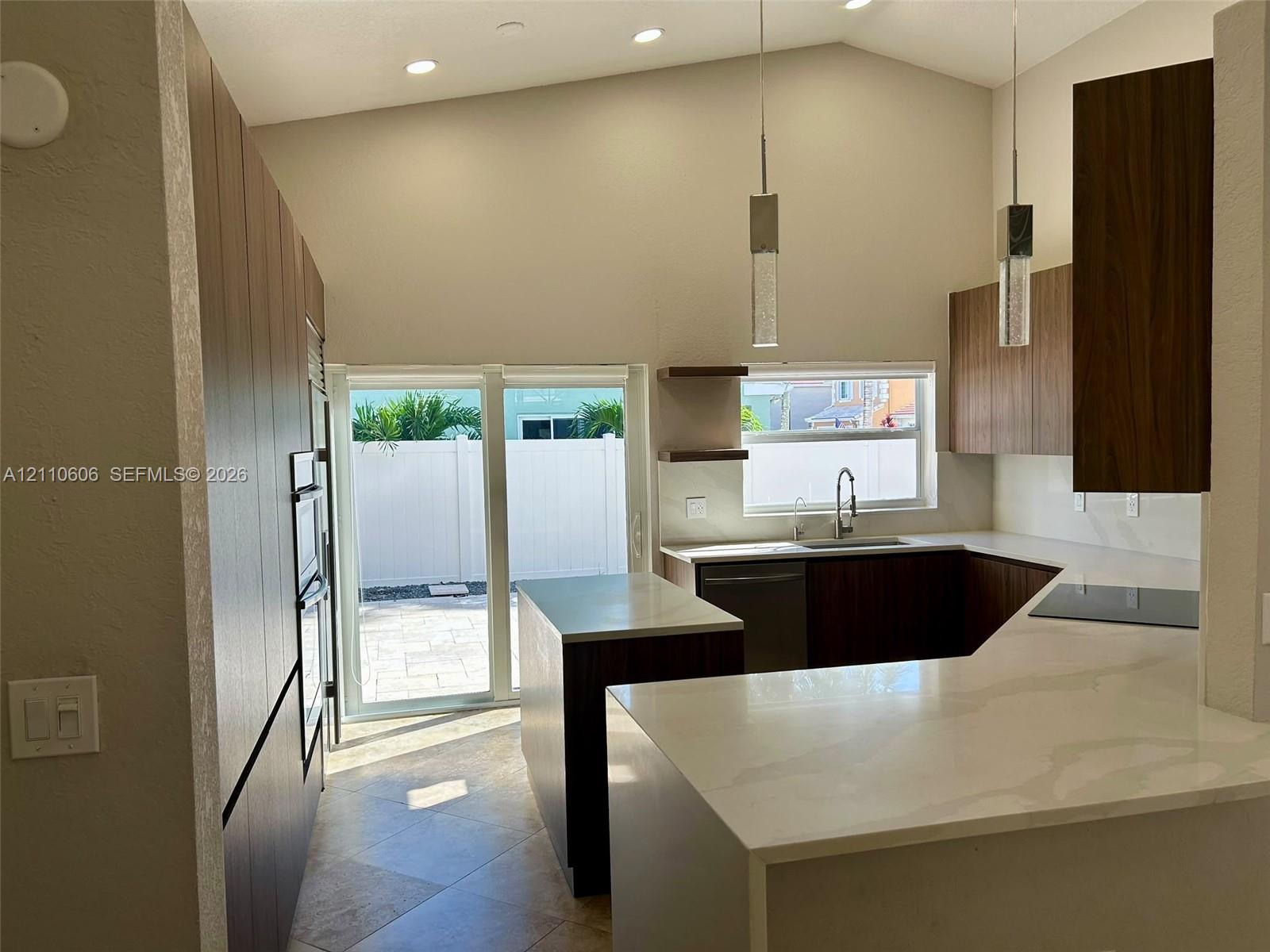 Kitchen featuring flat-panel cabinetry, stone-finish countertops, stainless steel appliances, vaulted ceilings, and pendant lighting
