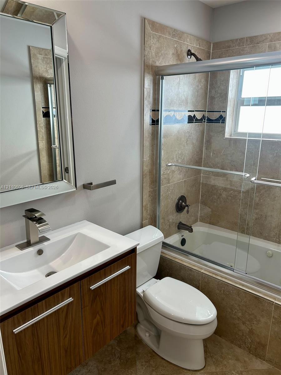Bathroom featuring a wood-finish vanity with a rectangular sink, beveled-edge wall mirror, and a tiled shower-tub combination with a sliding glass door
