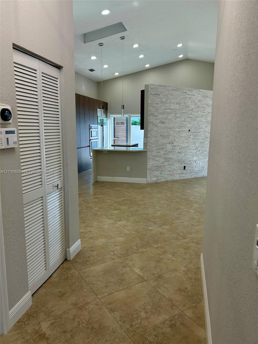 Open-concept space featuring vaulted ceilings, recessed lighting, a stone-veneer accent wall, tile flooring, and built-in cabinetry