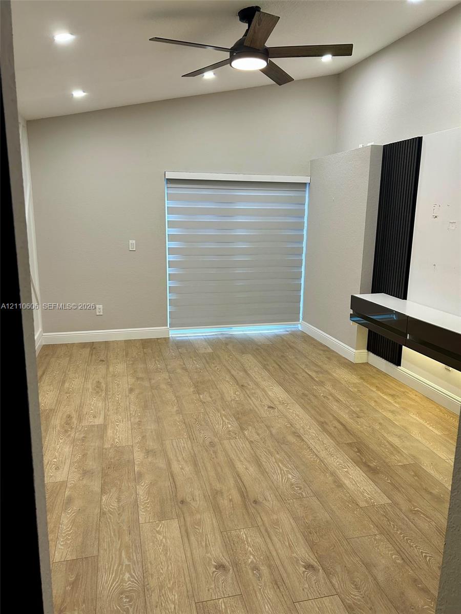 Wood-finish flooring, vaulted ceilings, recessed lighting, ceiling fan with integrated lighting, and a built-in media console featuring vertical accent paneling