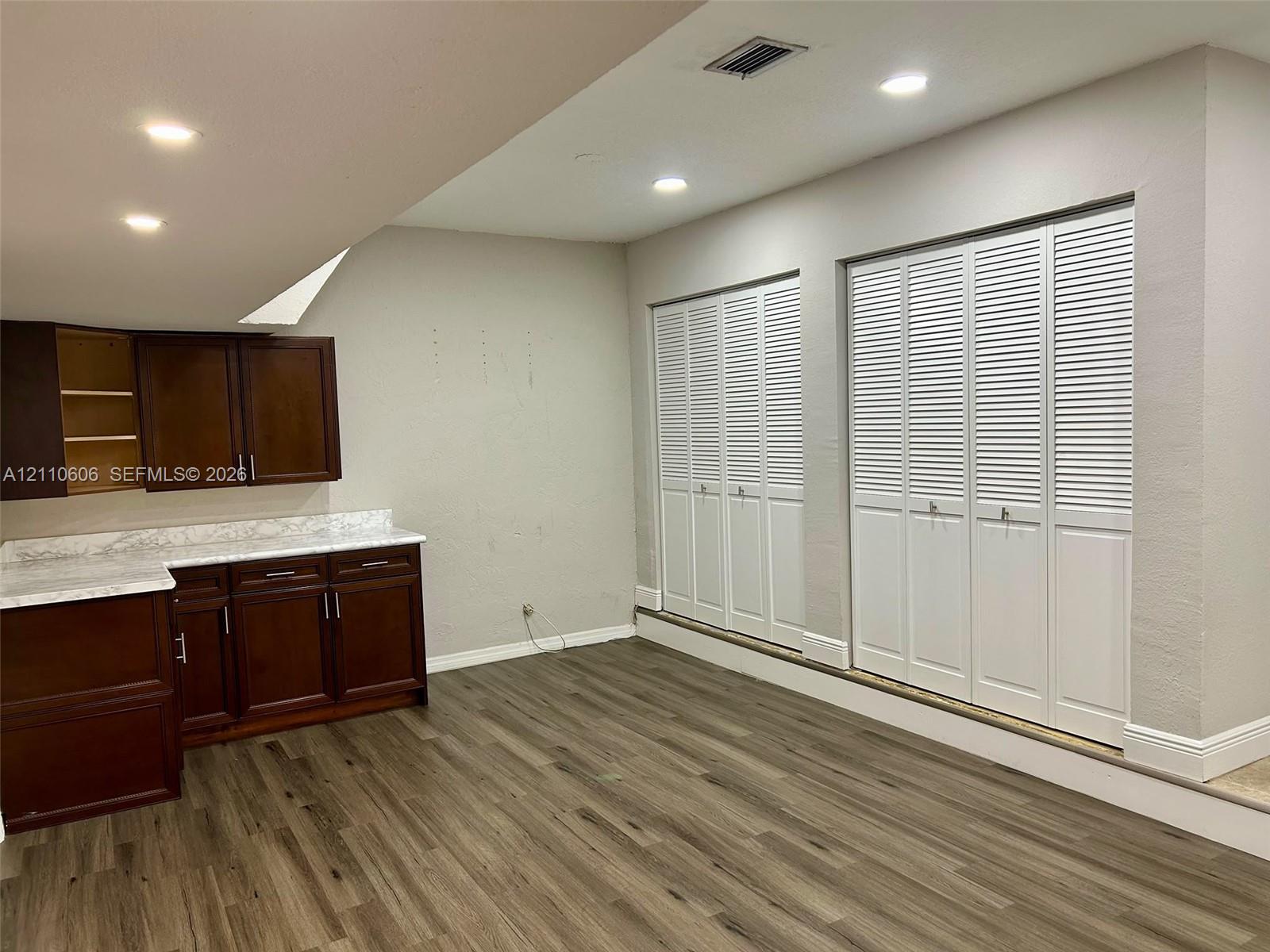 Wood-finish flooring, dark wood cabinetry with stone-patterned countertops, and dual white louvered-style closet doors