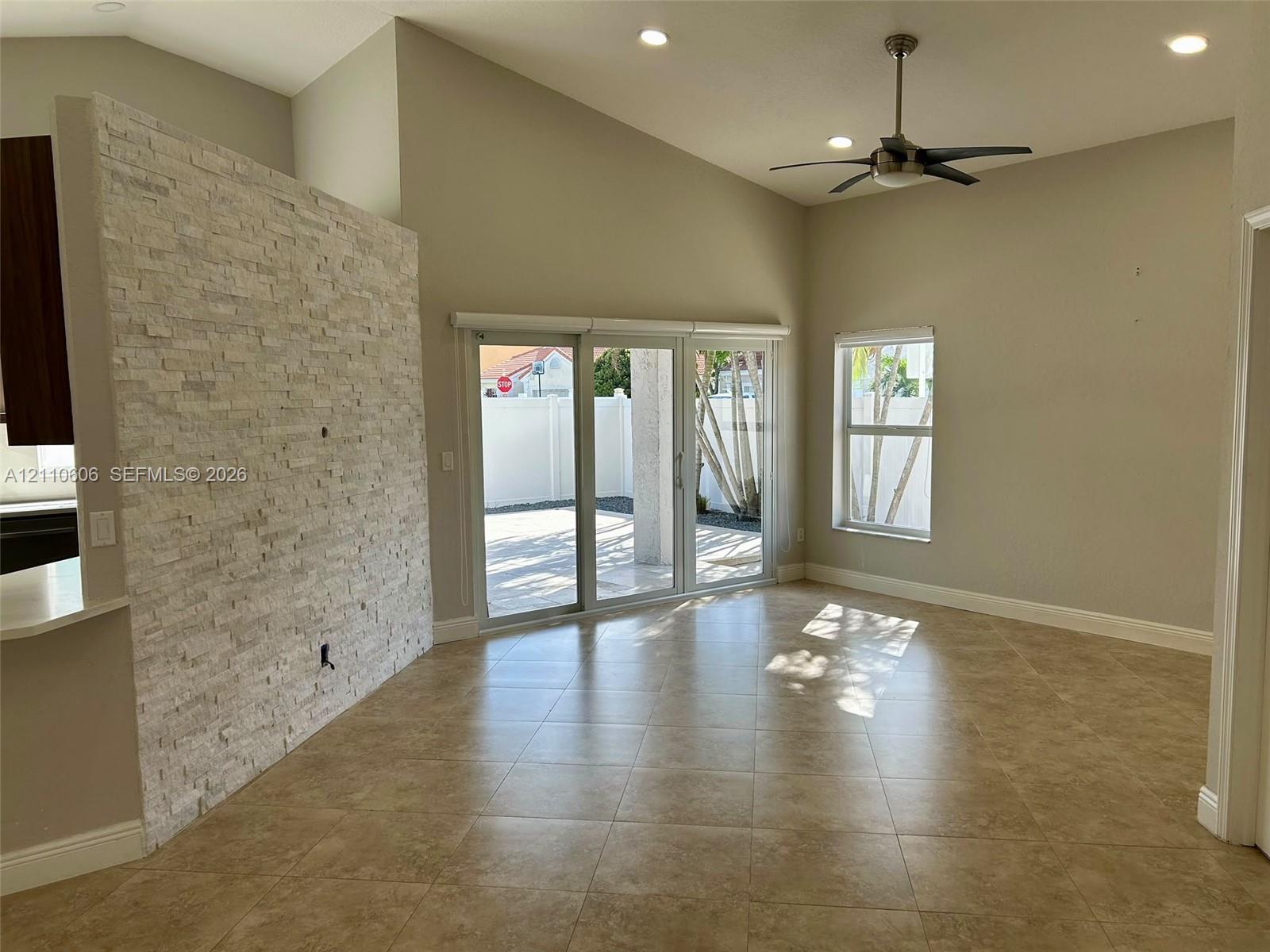 Vaulted ceiling interior featuring stacked stone accent wall, neutral ceramic tile flooring, sliding glass patio doors, and recessed lighting