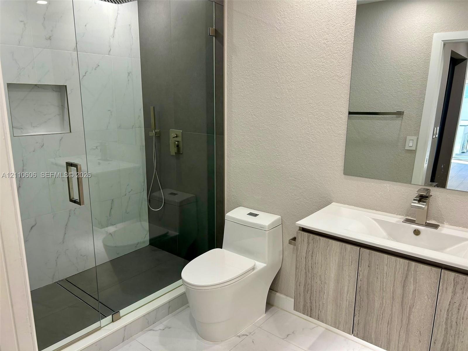 Walk-in shower with floor-to-ceiling tiled walls and a recessed niche, frameless glass enclosure, wood-finish vanity with an integrated countertop sink, and polished metal fixtures