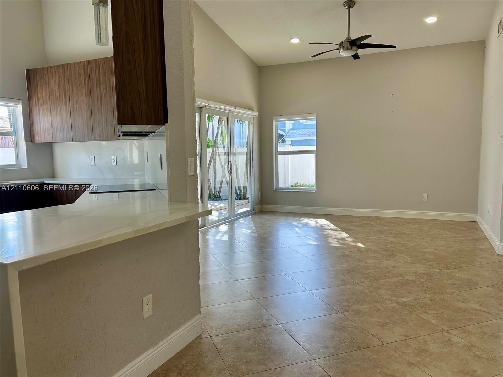 Open-concept interior featuring vaulted ceilings, neutral tile flooring, wood-finish cabinetry, white solid-surface countertops, and sliding glass doors