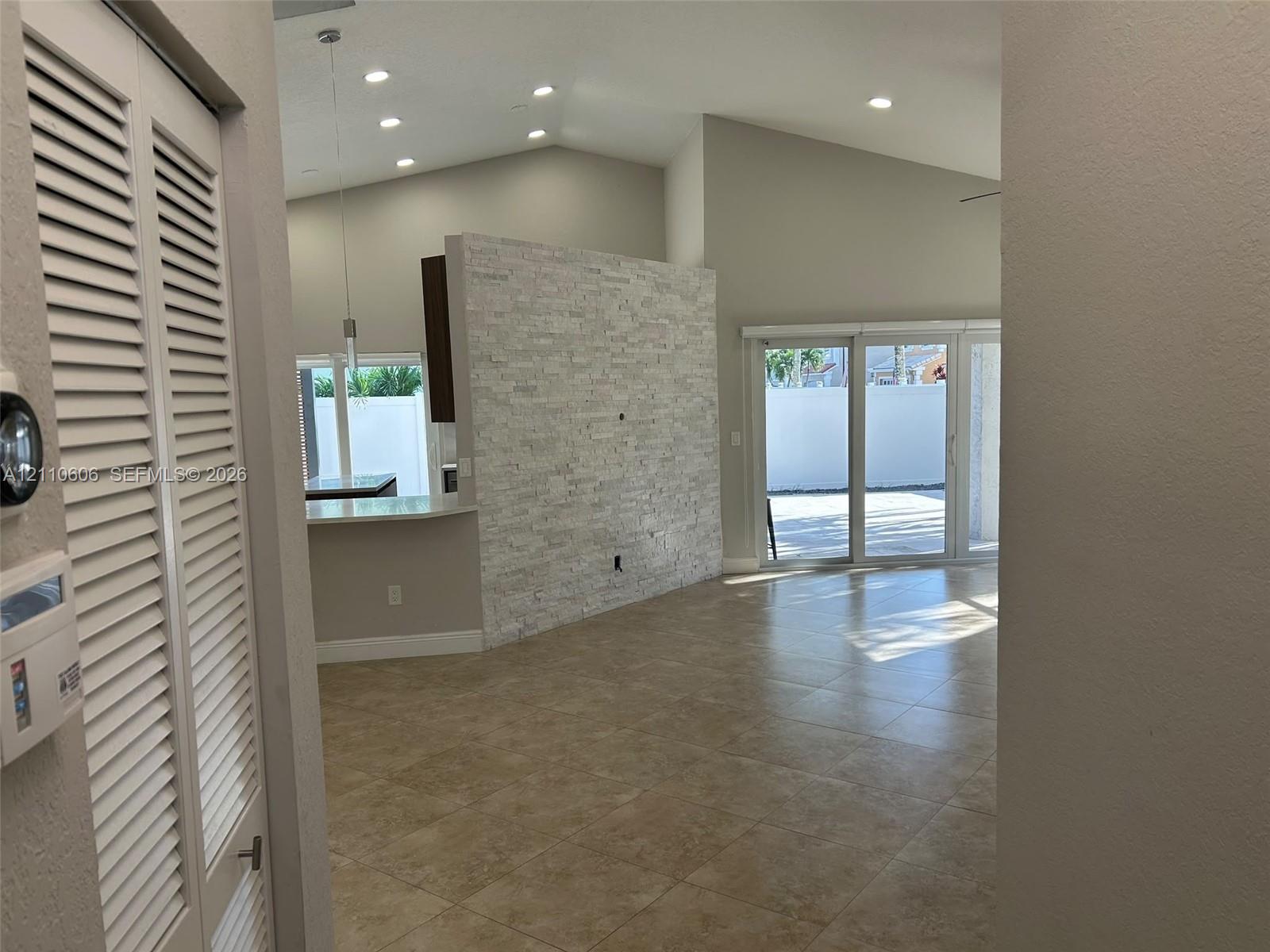 Vaulted ceilings featuring recessed lighting, a stone-finish accent wall, and large-format tile flooring, complemented by sliding glass doors leading to the exterior