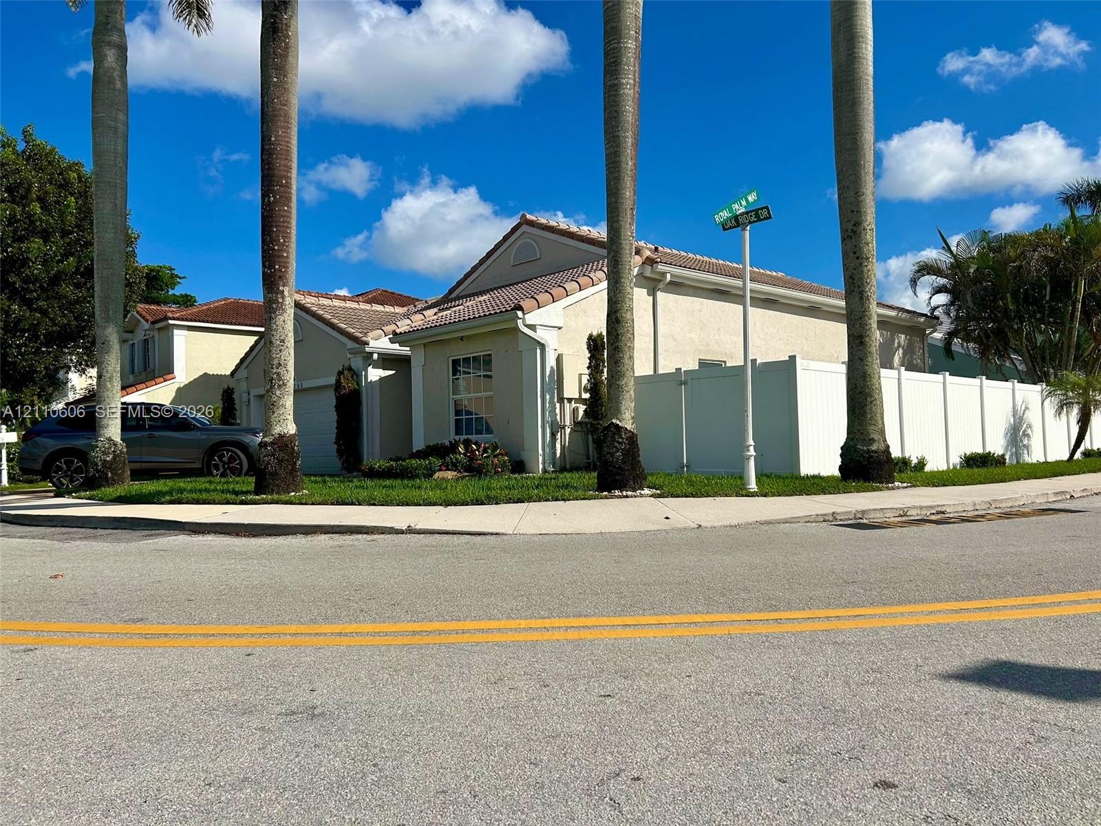 Stucco exterior featuring a tiled roof, concrete driveway, and white vinyl perimeter fencing Stucco exterior featuring a tiled roof, concrete driveway, and white vinyl perimeter fencing