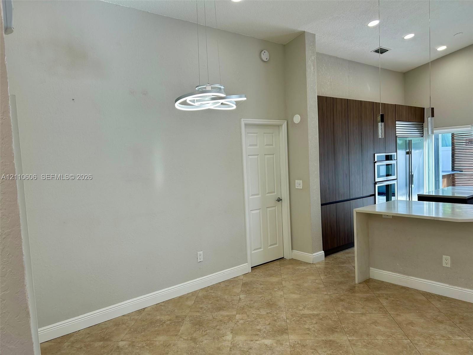 Vaulted ceilings featuring modern sculptural pendant lighting, stone-finish tile flooring, floor-to-ceiling wood-finish cabinetry, and recessed lighting