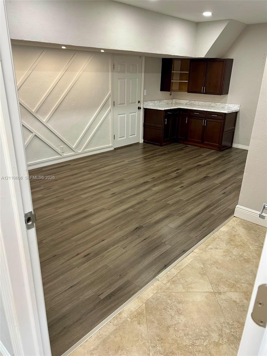 Geometric wall molding, wood-finish flooring, dark-stained cabinetry, light-toned stone-finish countertops, and recessed lighting