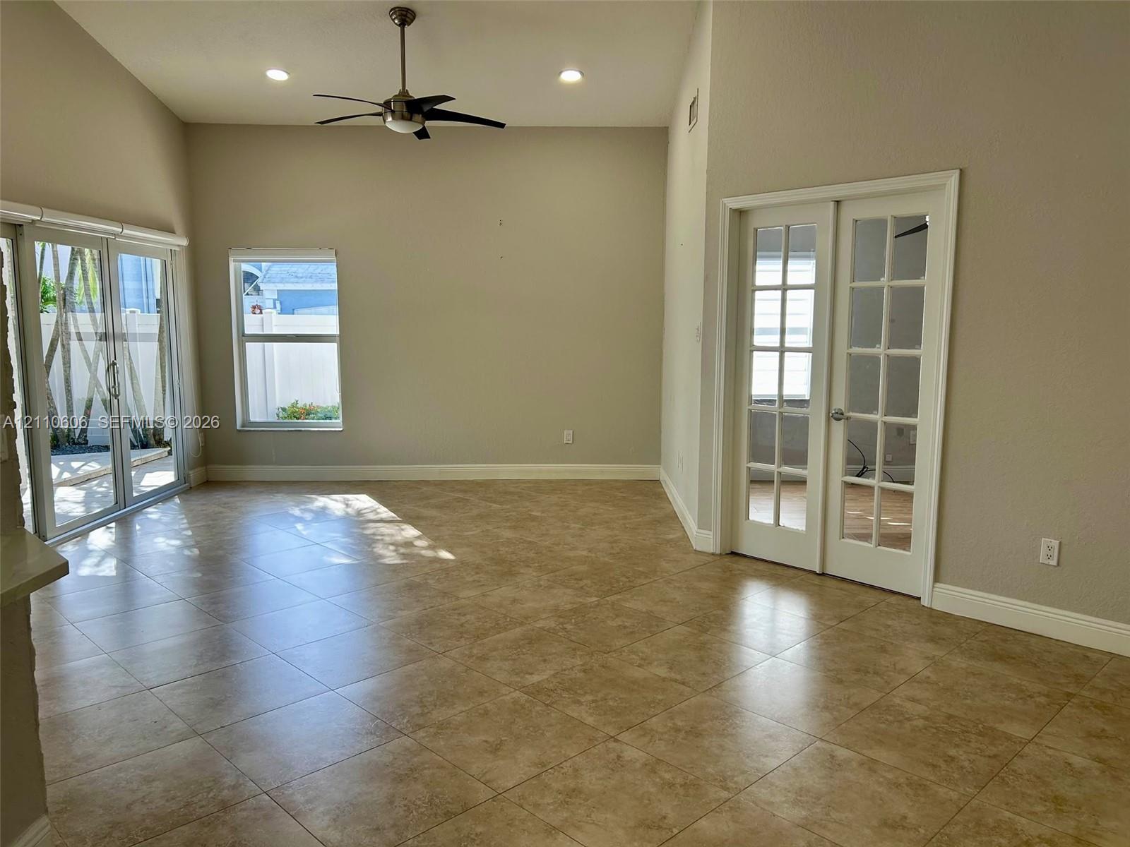 Vaulted ceilings featuring a central ceiling fan and recessed lighting, large-format tile flooring, and glass-paneled French doors