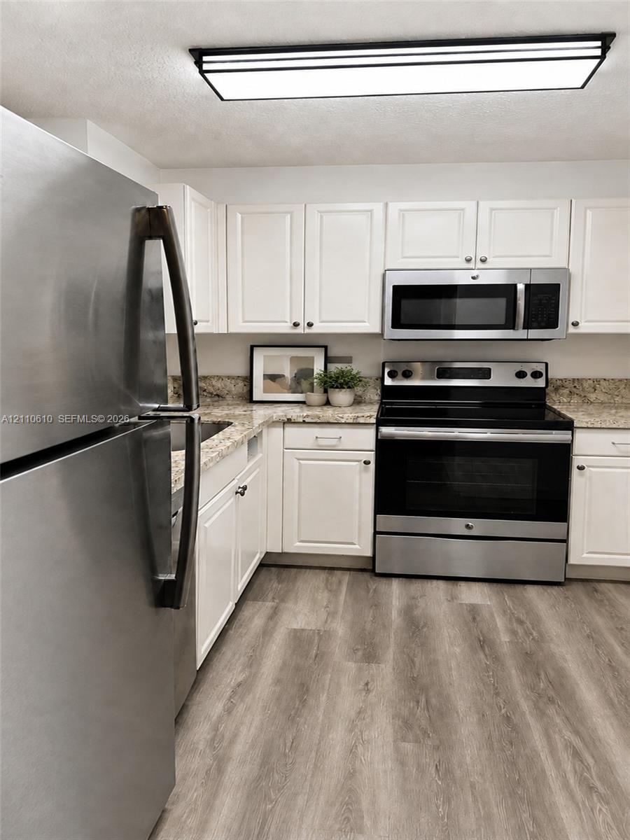 Kitchen featuring white cabinetry, stone countertops, stainless steel appliances, and wood-finish flooring