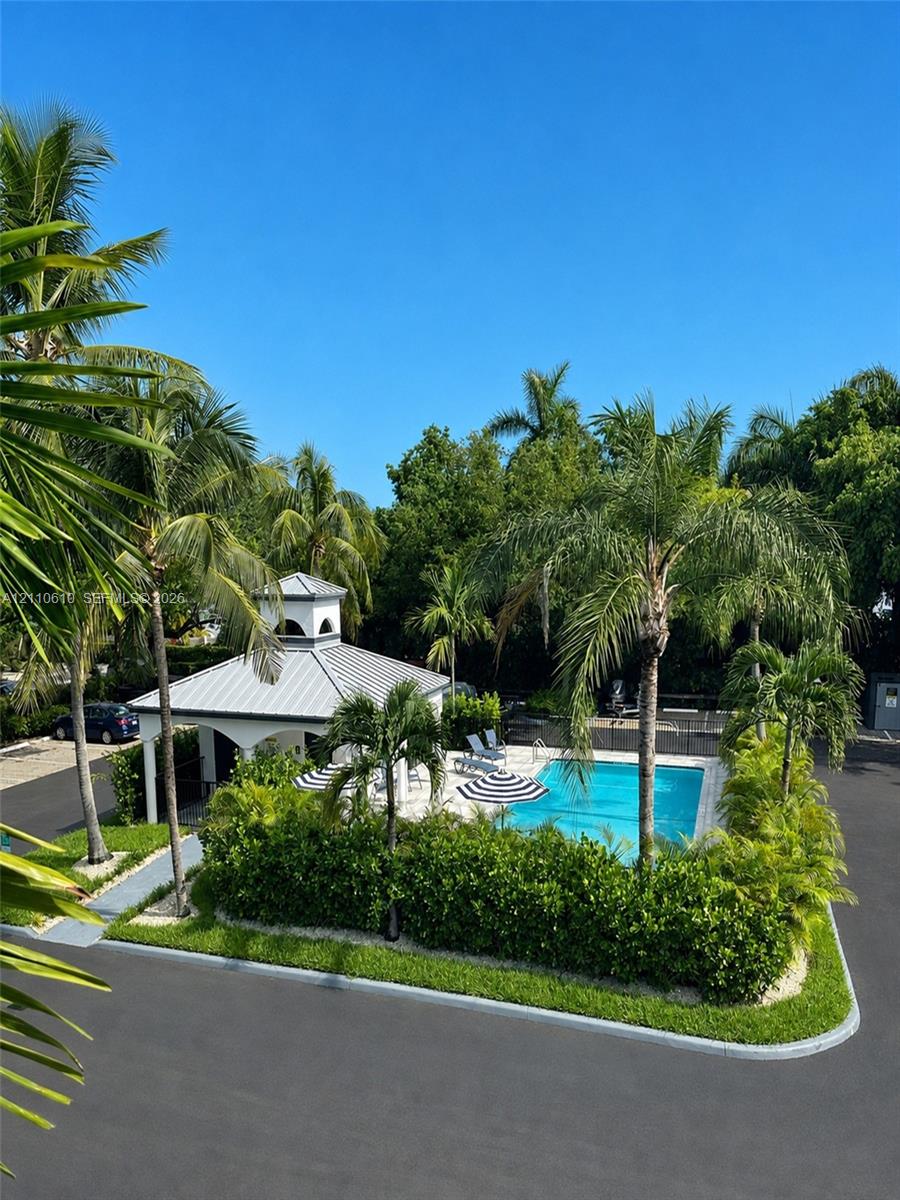 Swimming pool with paved surround, covered gazebo structure, manicured perimeter hedging, and established palm trees
