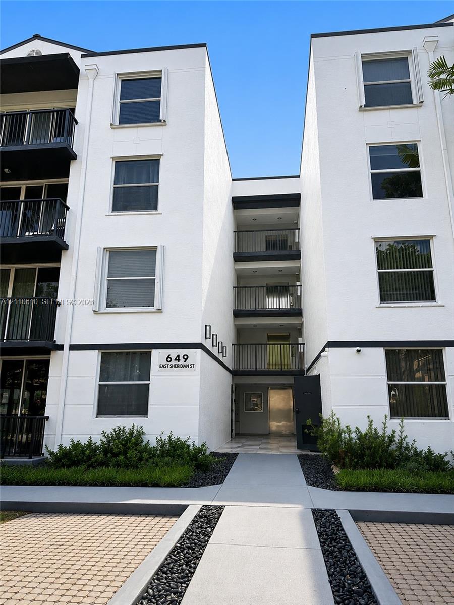 Modern multi-story facade with clean-lined exterior, vertical architectural interest, dark metal balconies, and geometric paved hardscaping