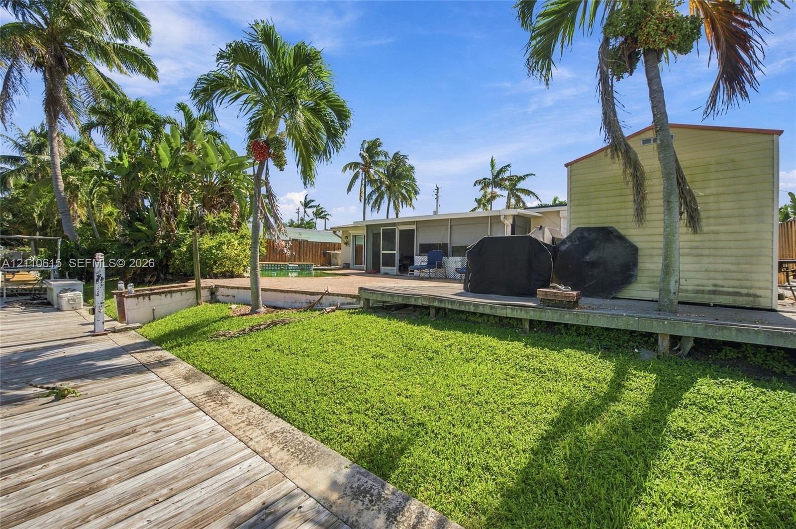 Outdoor space featuring a wooden deck, a grass lawn, a paved patio, and mature palm trees