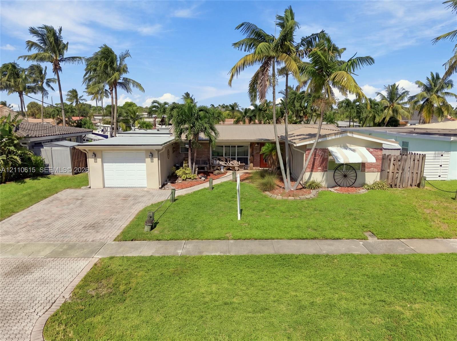 Single-story residence featuring a paved brick driveway, attached garage, stone facade accents, metal roofing, and mature palm landscaping