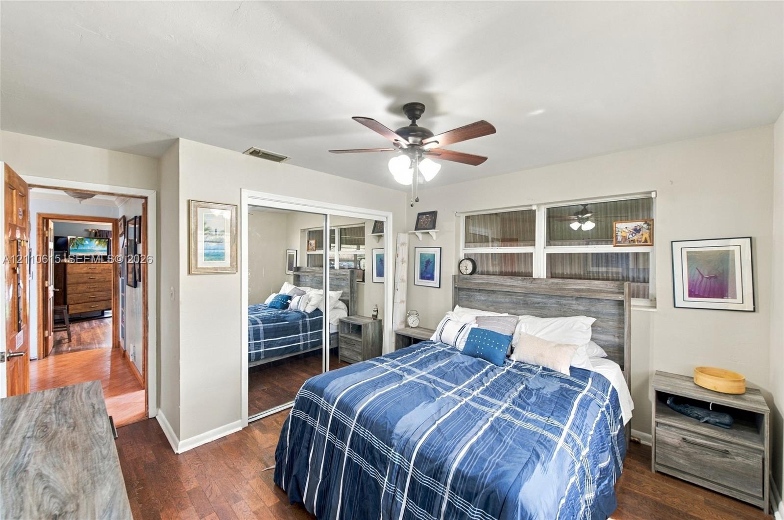 Room featuring wood-finish flooring, a ceiling fan with integrated lighting, and mirrored sliding closet doors