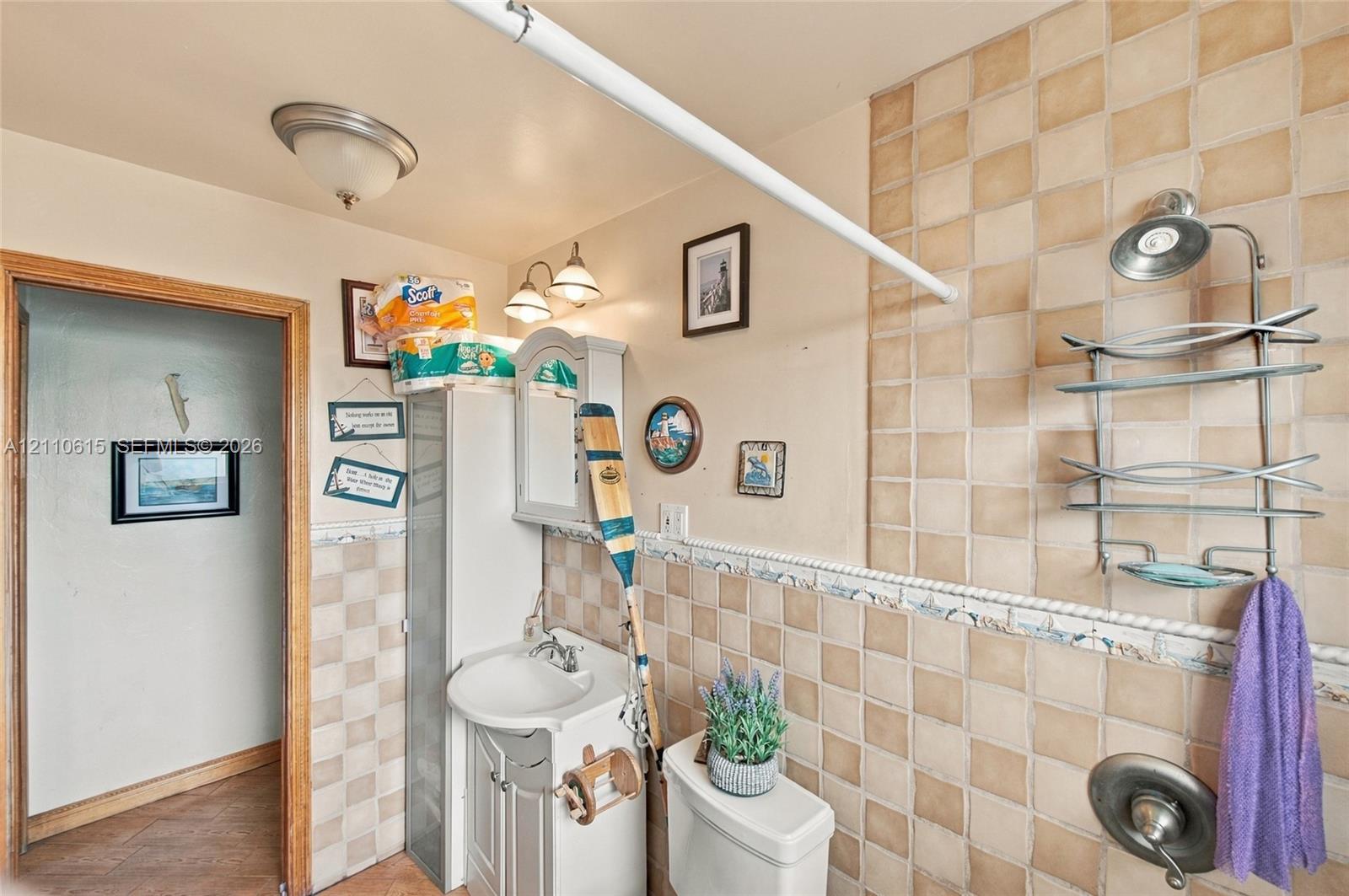 Bathroom featuring square ceramic wall tiling with a decorative border, pedestal vanity with a sink, built-in storage cabinet, and a single-handle shower valve