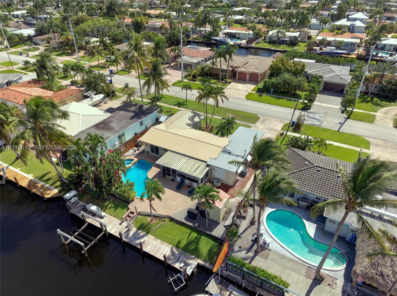 Waterfront property featuring a private boat dock, a concrete paved patio, an in-ground swimming pool, and tropical landscaping