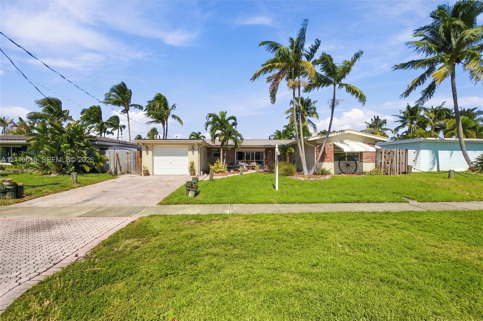 Single-story exterior featuring a brick facade, paved driveway, one-car garage, and established palm trees Single-story exterior featuring a brick facade, paved driveway, one-car garage, and established palm trees