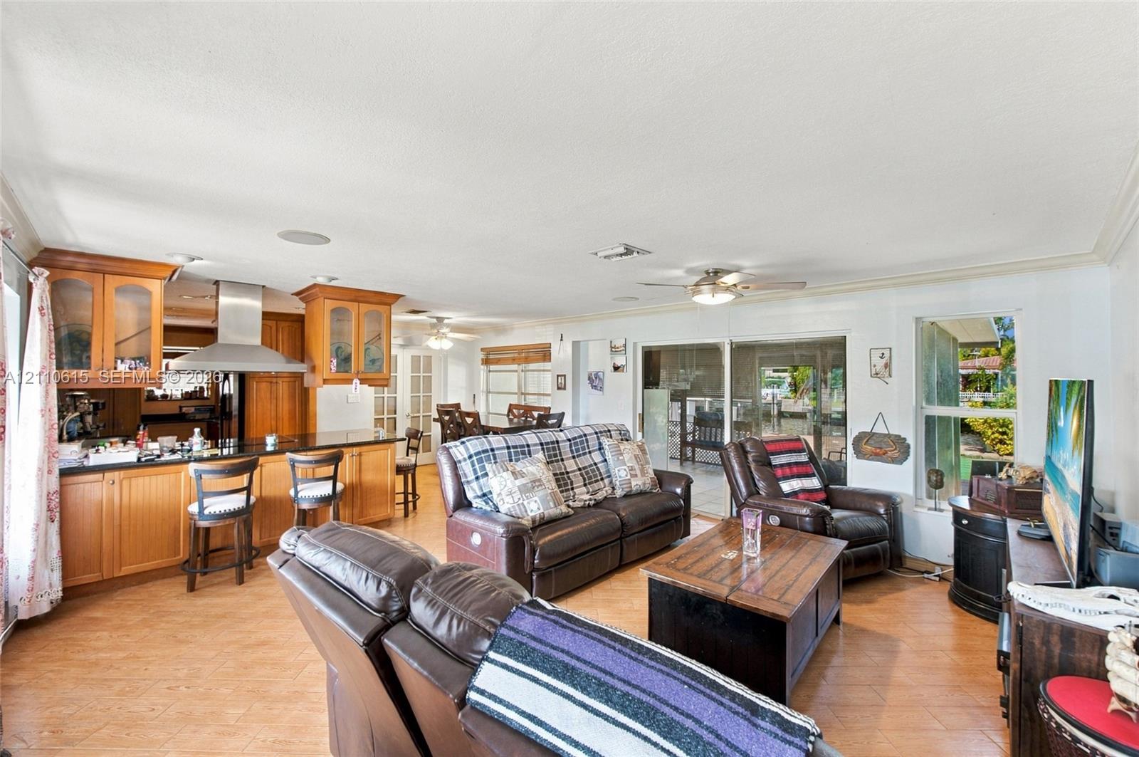 Open-concept interior featuring wood-finish cabinetry, a stainless steel range hood, tile flooring, recessed lighting, and sliding glass doors